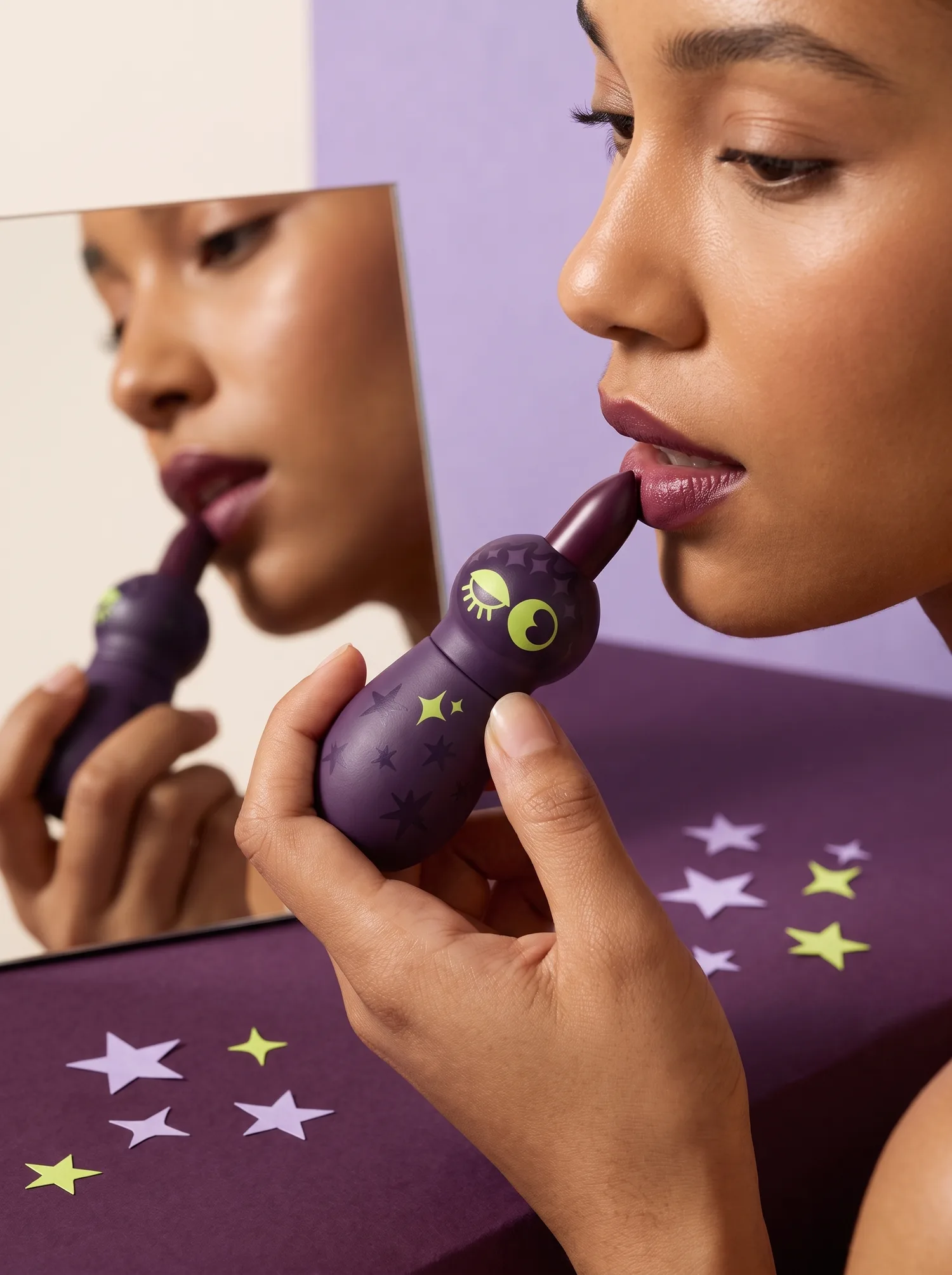 A model applying the bullet in a hand mirror, plum surface, paper stars