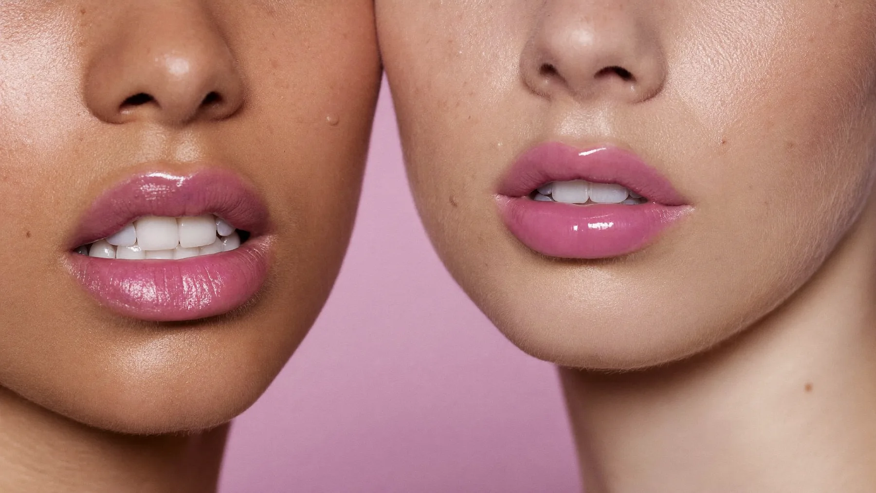 Two models cheek to cheek on a pink ground, both in glossy pink