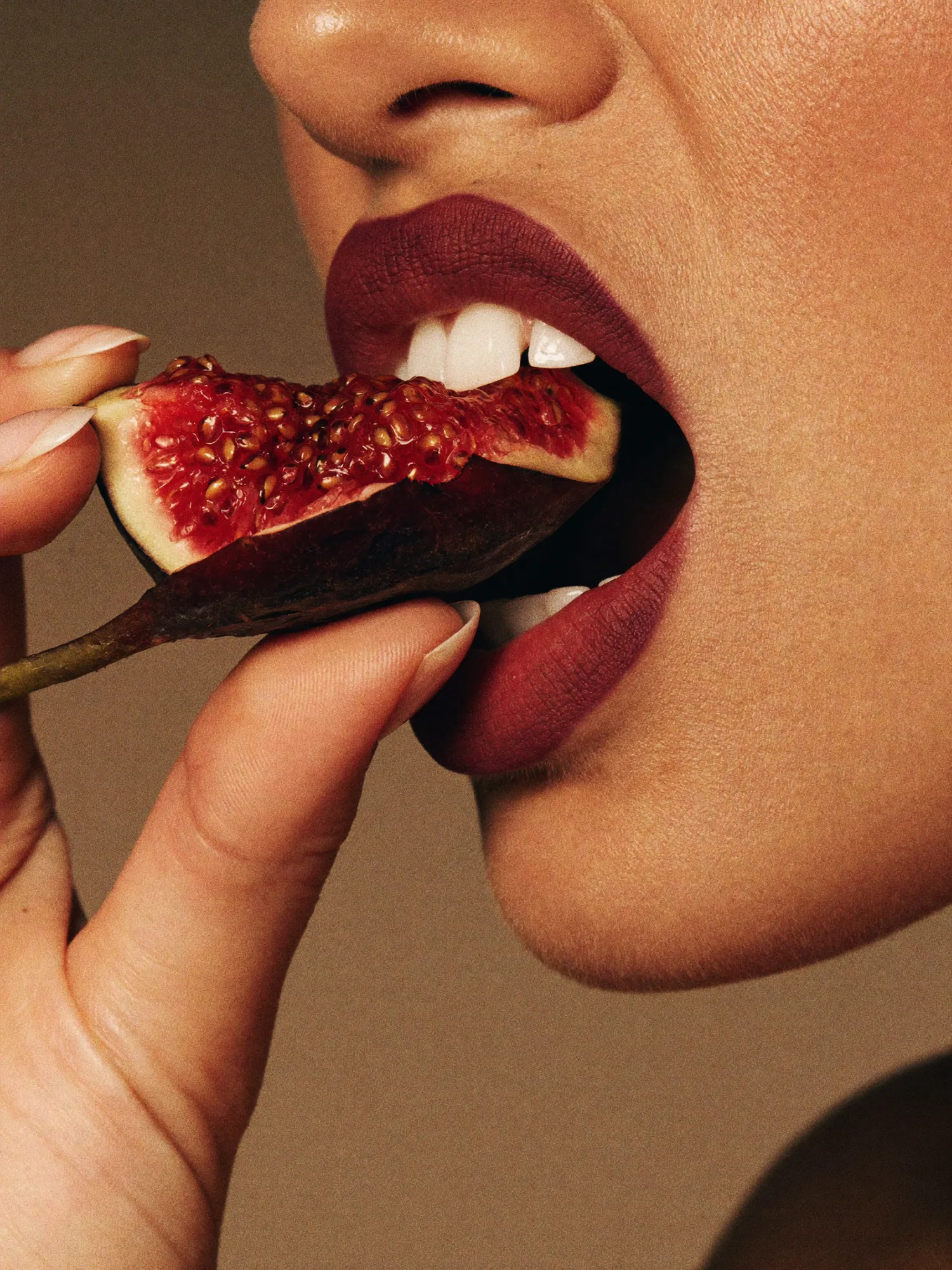 A fig held to the mouth, warm tan ground