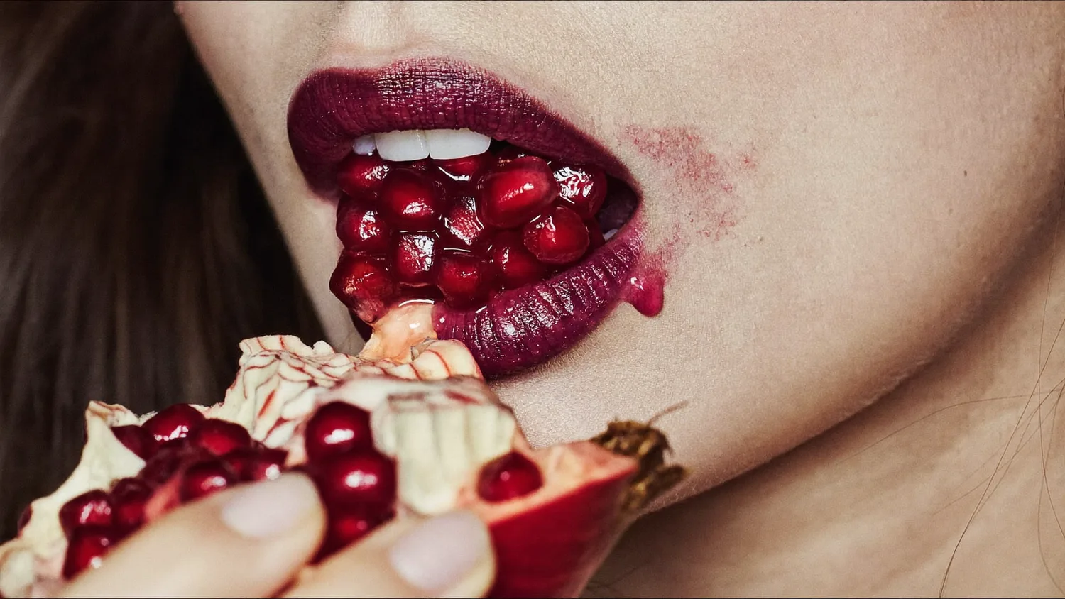 Pomegranate held to a stained lip