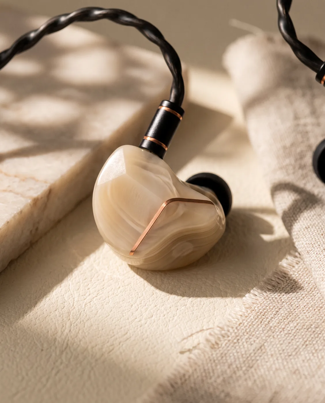 A NUMEN IEM resting on raw linen in low sun, the copper chevron catching the light