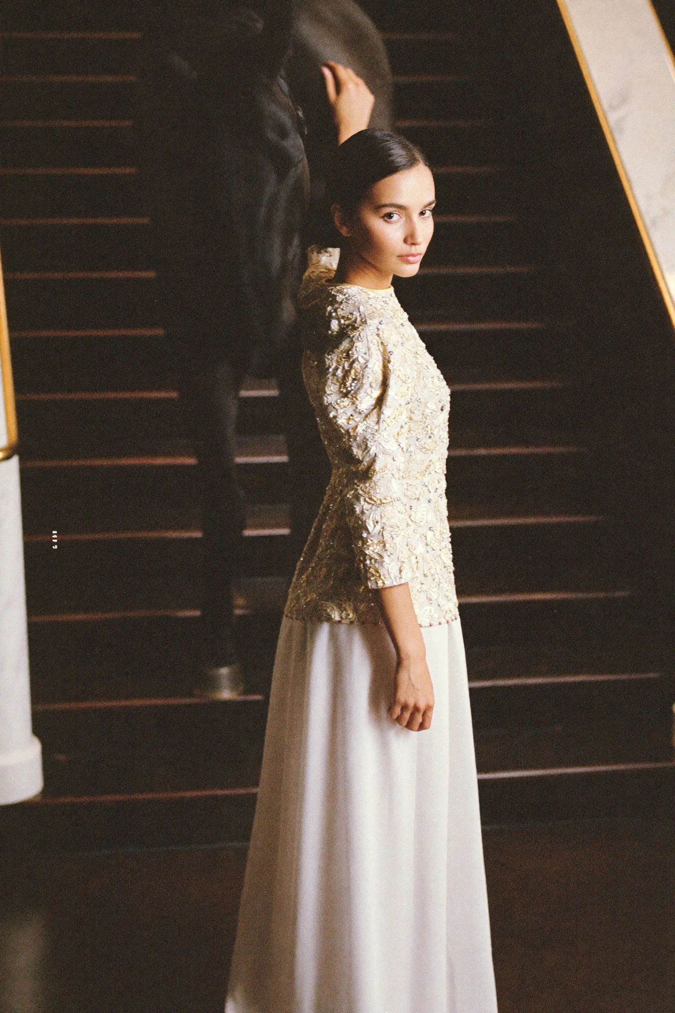 A gold and ivory piece on a dark staircase, turning back toward the camera
