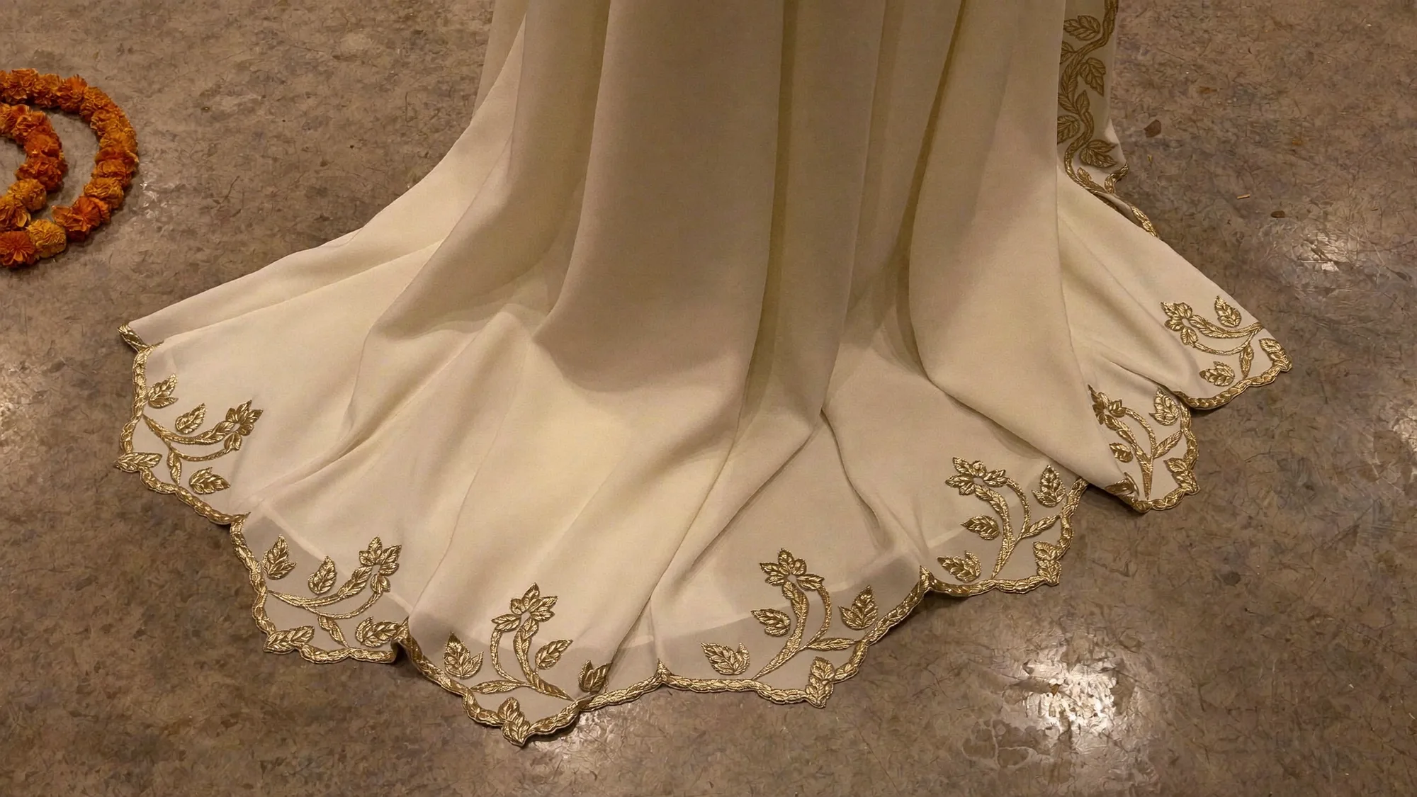 The scalloped hem of an ivory georgette dupatta worked in gold leaves, on stone